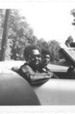 Dennis Edwards, front man of the Temptations, drives a car while an unidentified man sits in the passenger seat. Written on accompanying document: Edwards, Dennis (Temptations).
