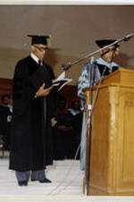 President Grant Shockley speaks from the podium in front of the 1978 graduation ceremony with Charles Copher standing behind him. Written on recto: Honorary Degrees 1978.