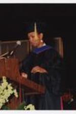 Mae Jemison, wearing a graduation cap and gown, standis at the podium at commencement.