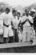 A group of demonstrators are shown standing around a casket with protest signs, one of which reads "We Don't Need A Racist Mayor So Beat It Emory Folmar".