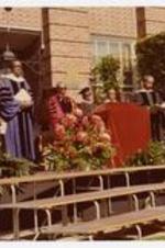 A view of men, wearing graduation gowns and caps, standing on stage at commencement.