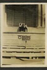 Three people sit in front of a stage behind sign "Do not stand on or place feet on marble benches."