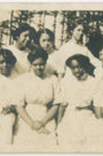 A group of eight women pose for a picture outside with woods in the background.