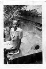 Unidentified woman sits on part of the hillside behind houses.