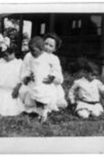 George A. Towns, Nellie Towns, and children play on the grass outside of a home.