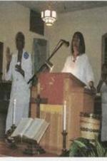 Rev. Yvonne McCoy and an unidentified woman speak to the congregation from behind the podium.