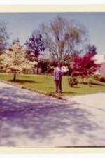 D. Hill standing in yard. Written on verso: Neighbor D. Hill at dogwood season. The driveway separates his stand and the house which is not viewed. Mr. Hill as one of the original neighbors made a most outstanding contributions til age took its toll.