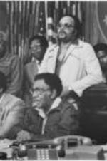 Southern Christian Leadership Conference President Joseph E. Lowery, Reverend Jesse Jackson, and others (including UAW representative Joe Davis, behind Lowery) are shown speaking at a Pilgrimage to Washington press conference in Tuskegee, Alabama. Written on verso: Press Conf. Apr. 19, '82. Tuskegee