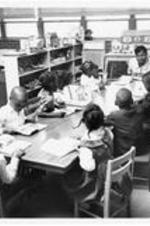 Children sit and study with a teacher in a classroom.