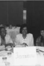 A group of women are shown at a table with an "International" sign at a national AIDS and Black Community conference.
