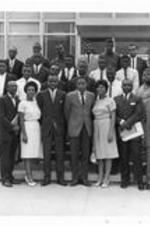 A group portrait of men and women standing on steps outside a building. Written on verso: Fall, 1963. Junior class - 1963/64 with Dr. Charles B. Copher (standing front, far left).
