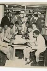 A group of men look at microscopes, papers, and a model of the human body in a laboratory. Written on verso: CC 1951, Beta Phi Zeta, (Biological Honor Society), L.H. Anderson (Pres.), Solomon Sears (Vice Pres.), Rufus Wilson (Secretary/Treasurer), Perry Mitchell (Parliamentarian), Homer Shipman (Chaplain).