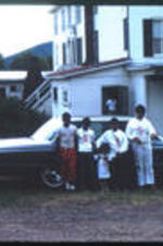 Children stand  in front of a car.