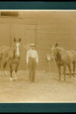 Unidentified man with two horses in front of barn.