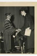 A man, wearing graduation cap and gown, shakes hands With James P. Brawley on stage at commencement.
