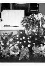 An unidentified man lies in a casket surrounded by flowers.