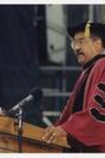 A man, wearing a graduation cap and gown, stands at the podium at commencement.