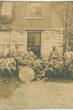 A group of unidentified musicians sit outside holding their instruments.