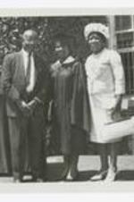 A man and two women pose on an outdoor stage at commencement.