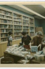 Three unidentified people work in an office surrounded by books.
