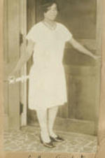 A woman stands in front of a door holding a diploma. Written on recto: College graduate.