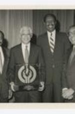 Elias Blake Jr. poses with three other men and a large glass award at an award presentation.