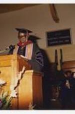 Indoor view of a man at podium in graudation cap and gown.