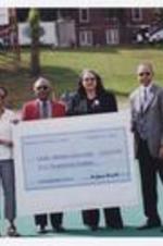Dr. Walter Boradnax poses with another man and two women holding a large check "Midtown Urology Center, October 12 2002, Pay to Clark Atlanta University $10,000," on football field.