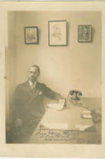 Edgar G. Brown sits at his desk holding a sheet of paper. Written on recto: To Irvin Henry McDuffie; A True Friend; with sincere esteem Edgar G. Brown.