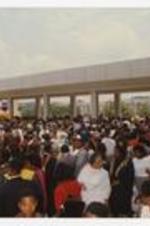 A large crowd of people gathered outside, including graduates wearing graduation caps and gowns.