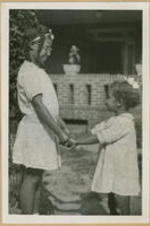 A young girl stands with a toddler and hold hands outside the home.