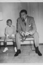U.S. Representative Adam Clayton Powell, Jr. is shown seated with a young boy. Written on verso: Adam Clayton Powell