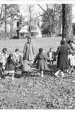 Children hold hands in a circle on the playground lawn.