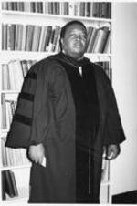 Portrait of C. Eric Lincoln in commencement regalia standing in front of a bookshelf.