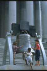 Anna Henderson and the Henderson children observing a bell on the steps of an unidentified building.