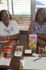 Two unidentified women from the Fulton County Department of Heath &amp; Wellness sit at a table with health information brochures and magazines at a Pampering For Peace event held at D'Lor Salon &amp; Spa in Atlanta, Georgia in recognition of National Domestic Violence Awareness Month.
