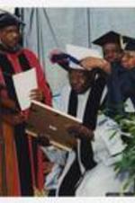 Hank Aaron receives an award at the podium at commencement from a woman and another man as Thomas W. Cole, Jr. looks on.