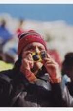 A woman, wearing a beanie hat "Clark Atlanta", holds a disposable camera, surrounded by other men and women.