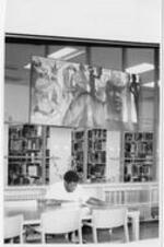 A man studies at a table inside the library under a large painting.