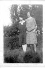 Two women stand outside in a yard.