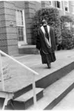 James P. Brawley walks towards a building wearing a commencement robe.