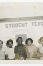 Group portrait seated in front of sign "Your Student Teacher".