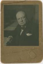 Winston Churchill sits at a desk. Written on verso: Souvenir [?] 1942. Written on verso: Winston Churchill sent all the White House staff domestic and other wise a photo of himself after his visit. Lizzie McDuffie.