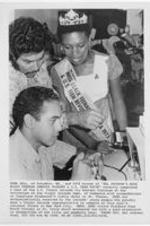 Edna Hill, the winner of the Miss Black Teenage America pageant, observes an employee working on a wristwatch. Caption on photo reads: Edna Hill, of Columbia, MD., and 1974 winner of "Hal Jackson's Miss Black Teenage America Pageant &amp; U.S. Teen Revue" recently completed a tour of the U.S. Virgin Islands via Eastern Airlines at the invitation of the Virgin Islands Dept. of Commerce with accommodations at luxurious Bluebeard's Castle Hotel in St. Thomas. Edna was enthusiastically received by the islands' young people who proudly sent a Virgin Islands representative to compete at this year's national finals in New York City. Here, Edna visits a Standard Time Watch Factory in St. Croix which presented her with a gold wristwatch in recognition of her title and goodwill tour.