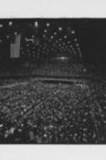 A wide view of a crowd in an auditorium is shown at what may be a Black Expo event in Chicago, Illinois. Black Expo was a fair that exhibits the achievements of black culture, business and industry to the public. It was originally engineered and sponsored by the Southern Christian Leadership Conference (SCLC) in the 1960s. Written on verso: Chicago Black Expo, 70?