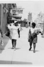Three women walk down a city sidewalk.