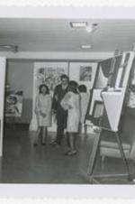 Two women and a man stand in the middle of an art exhibit.