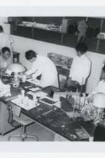A man works with four young women at a laboratory table with trays and other science equipment in a classroom.