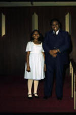 An unidentified girl stands next to an unidentified man, possibly her father.