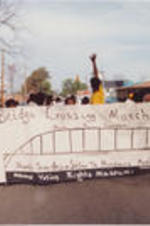 Demonstrators are shown marching with a "Bridge Crossing March" banner.
